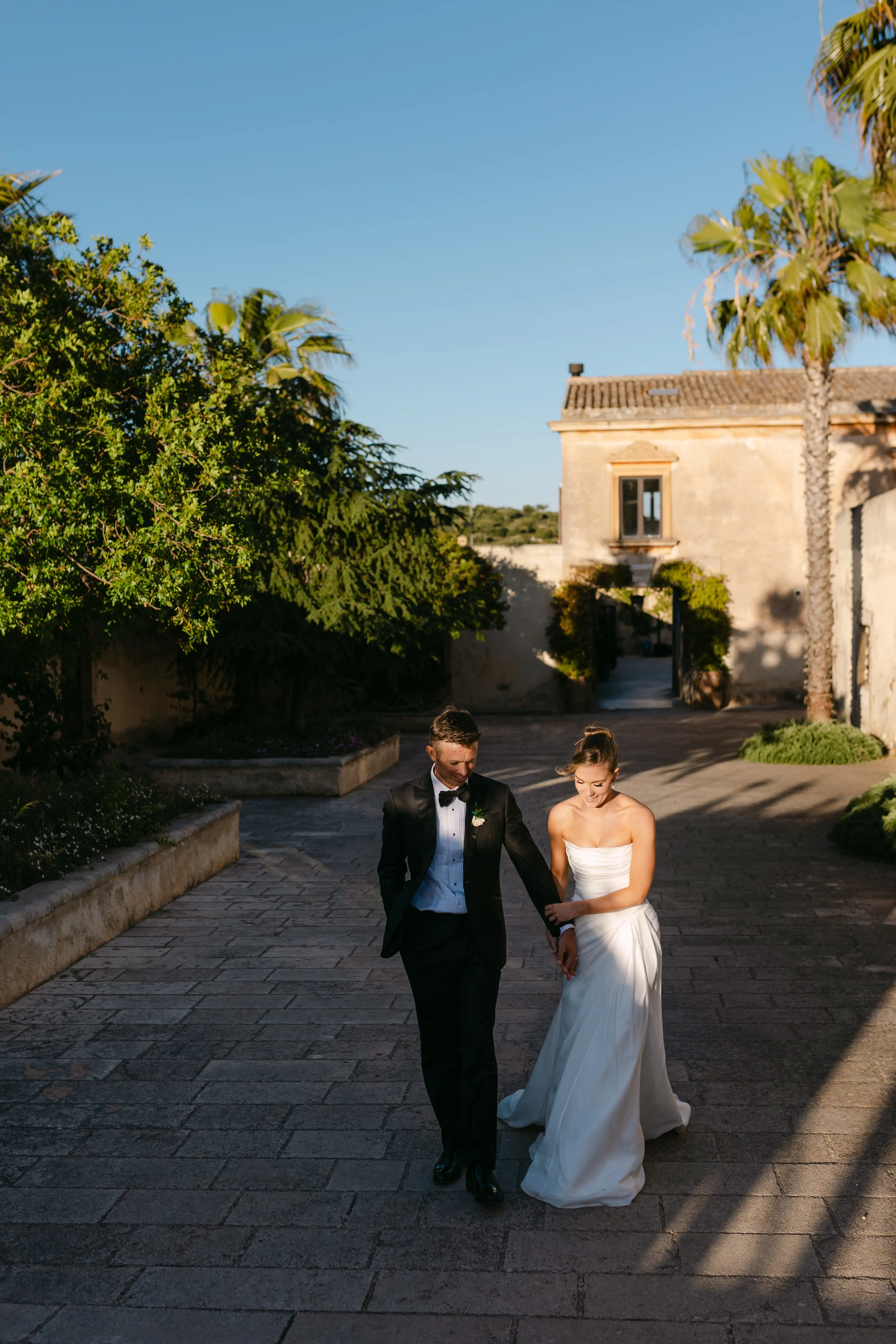 Bride and groom walking together through a historic Italian villa courtyard at golden hour.